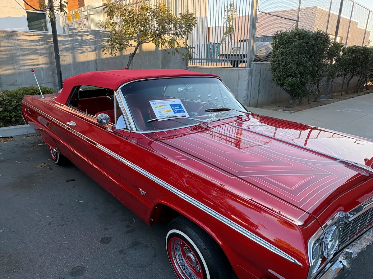 A vintage, red Chevrolet Impala car with the Stampe Encore envelope on the windshield